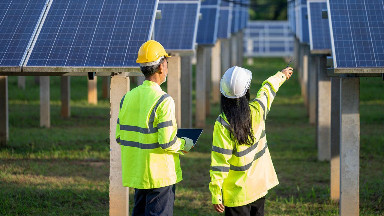 Two engineers in hard hats with laptop discuss solar panels